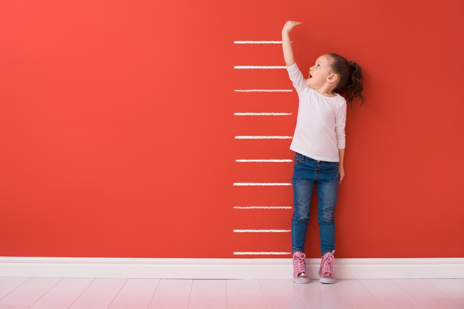 Child measuring height against a ruller on the wall as a growth chart
